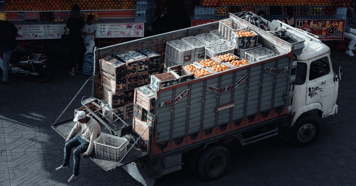 A truck loaded with crates of oranges parked at an urban market scene during daytime.